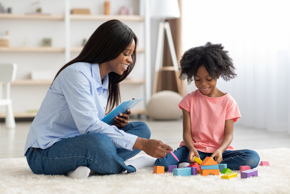 Adorable black kid and child psychotherapist playing with bricks child psychiatry care service in San Diego