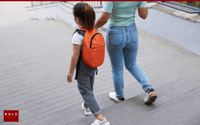 Child with backpack walking beside an adult on a city sidewalk, symbolizing support and guidance.