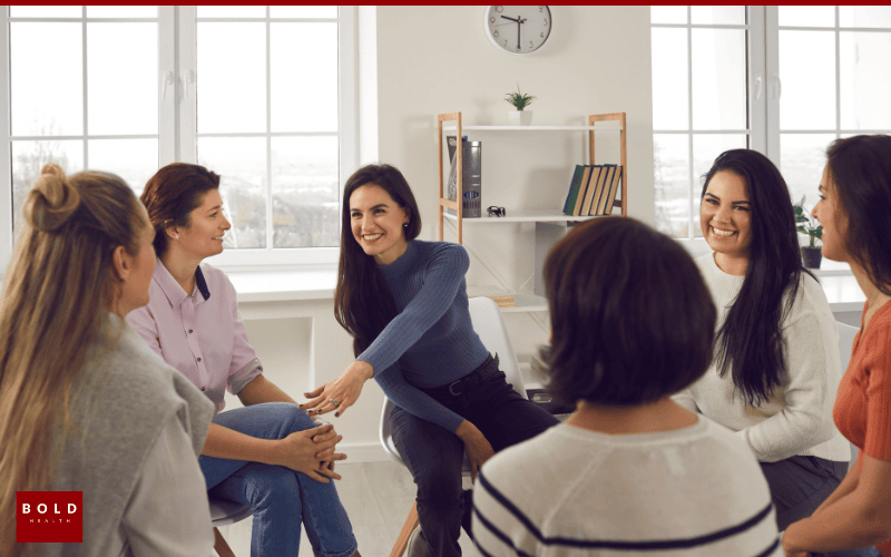 Women participating in a group therapy or support session in a well-lit, modern room with large windows.