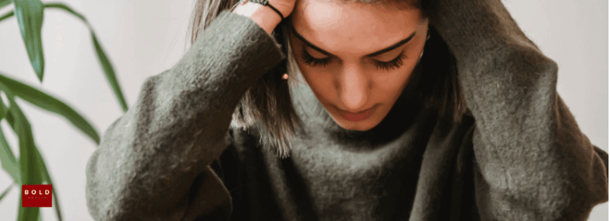 Young woman with head in hands, experiencing stress or mental health challenges, in a home setting.