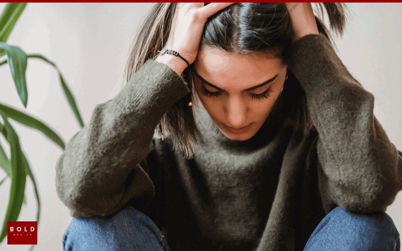 Young woman with hands on her head, showing stress and anxiety, in a casual setting.